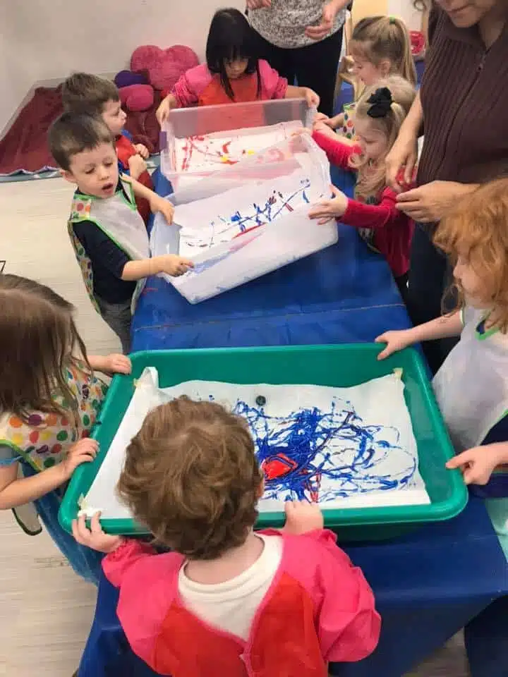 Children painting in trays at a classroom table